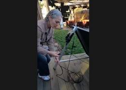 Person kneeling on a wooden deck, adjusting an outdoor satellite dish antenna mounted on a stand with cables nearby.